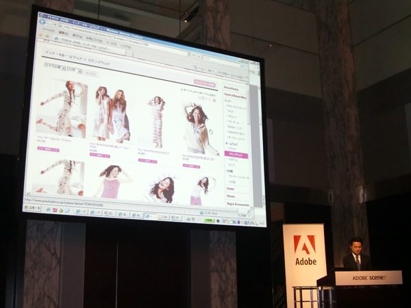 Adobe Scene7の導入について紹介する、株式会社ピーチ・ジョン執行役員 守安智氏。導入動機について、ユーザからの多様なニーズへの対応、リッチな体験の提供、カタログのアウトソース費の削減など、さまざまなメリットについて述べた。